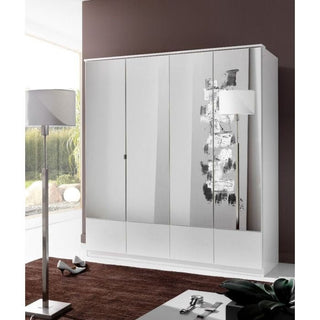 The CHOICEWARDROBE Inagu 4 Door Mirrored Wardrobe – 180cm Wide, White High Gloss stands against a brown wall beside a tall floor lamp. The room also has a brown rug, shoes, and a window showing greenery outside.