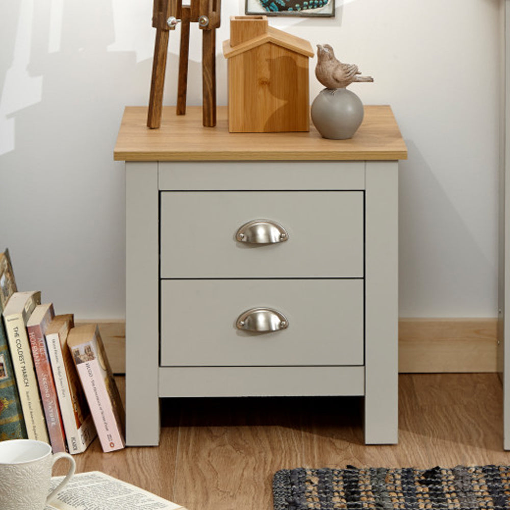 Loftus grey wooden bedside cabinet with oak top and two drawers, featuring decor and books.