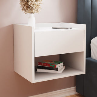 White wooden wall-hung bedside cabinet with drawer and shelf, holding books and dried flowers.