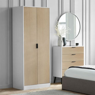 A modern UK bedroom features the CHOICEWARDROBE Akron Wooden Wardrobe in a stylish two-tone white and oak finish with black handles, plus a matching chest of drawers, round mirror, decorative vases, and a gray upholstered bed.