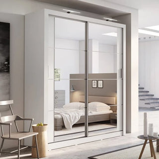 A modern bedroom features the CHOICEWARDROBE Allen Wardrobe, a 2-door sliding wardrobe with matt white mirrored doors. The reflection reveals a bed with white bedding, a nightstand, wall-mounted lights, and neutral minimalistic decor.