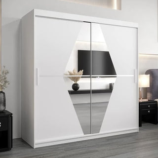 The Beloit Mirrored Wardrobe 2 Sliding Doors 200cm In White stands on a gray floor, featuring a central geometric mirror design. In the background, bedroom furniture including a TV and vase with dried flowers adds to the decor.