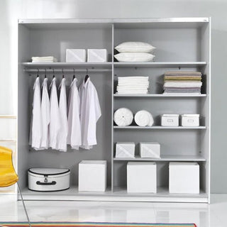The Biloxi Mirrored Wardrobe 2 Sliding Doors 221cm in Monastery Oak stands against a light gray wall, organized with white shirts, folded towels, storage boxes, pillows, and a suitcase. A yellow chair is placed to the left.