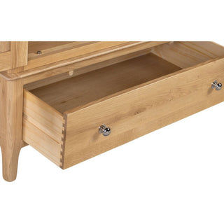 A close-up of the Callia Wooden Wardrobe With 2 Doors 1 Drawer in Natural shows its solid oak drawer partially open, featuring metal knobs and dovetail joints—ideal for adding stylish storage to your bedroom.