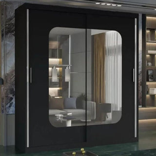 The CHOICEWARDROBE 120cm Sliding Door Mirrored Wardrobe in matt black with a central rounded mirror stands in a contemporary room, reflecting a sofa, cushions, and window with brown curtains. Sleek vertical handles adorn each door.