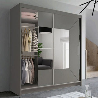 The CHOICEWARDROBE 120cm Sliding Door Mirrored Wardrobe in matt grey with a geometric panel and central mirror stands partially open, showing folded clothes, hanging shirts and jackets, and a potted plant. A staircase and modern light are visible behind.