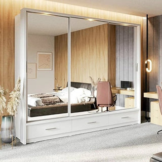 A modern bedroom with a CHOICEWARDROBE Aliso 250cm 3 Door Sliding Mirrored Wardrobe in matt white, LED lighting, and 3 drawer storage. The space also has a bed, desk, chair, wall art, plants, and wooden and gray accent walls.