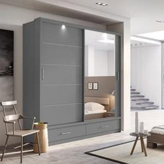 The CHOICEWARDROBE Aliso 3 Door Mirrored Sliding Wardrobe in matt grey with LED lighting and three drawers stands in a bright room. Its full-length mirrored door reflects a bed and pictures, enhancing both bedroom style and storage. A chair and table are nearby.