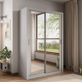 The CHOICEWARDROBE Allen 150cm Grey Sliding Wardrobe with full mirror doors is a compact, modern storage solution placed by a window with beige curtains; its mirrors reflect trees, while a potted plant and picture frame sit nearby.