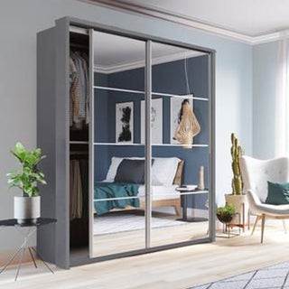 A modern bedroom with the CHOICEWARDROBE Allen 2 Door Mirrored Sliding Wardrobe in a grey finish, bed, wall artwork, armchair, potted plant, cactus, and ample natural light from a window.