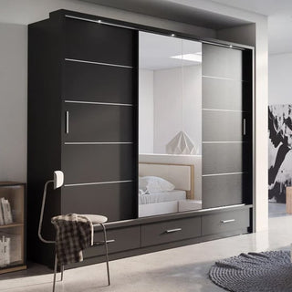 The CHOICEWARDROBE Allen 3 Door Sliding Wardrobe in modern matt black stands against the bedroom wall, featuring a full-length mirrored door that reflects a bed with a white headboard. It includes internal shelves, hanging rails, and three drawers.