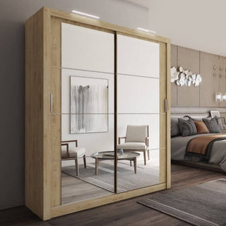 A CHOICEWARDROBE Allen Oak 2 Door Sliding Mirrored Wardrobe (181cm, modern design with LED lights & storage shelves) stands in a contemporary bedroom, its mirrored doors reflecting neutral-toned chairs, a round table, and abstract wall art.