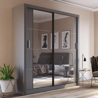The CHOICEWARDROBE Allen Wardrobe 150cm in Graphite Grey stands against a beige bedroom wall, its 2 sliding mirrored doors with LED lighting and adjustable shelves reflecting the bed, art, and furniture, with a potted plant nearby adding greenery.