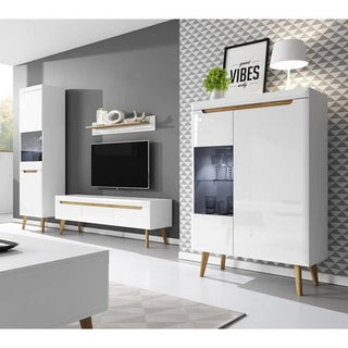A modern living room features white and wood furniture including a TV stand, tall cabinet, sideboard with lamp, plant, and print. A geometric wall pattern complements the CHOICEWARDROBE Alora 2 Door 2 Drawer High Gloss Wardrobe in white with oak legs.