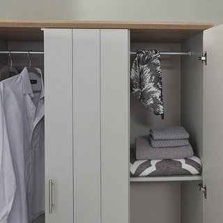 The CHOICEWARDROBE Alverton 3 Door Wardrobe in grey with an oak effect top and drawers features a hanging rod holding a button-up shirt and scarf, plus a shelf below neatly stacked with three folded towels or blankets. Silver handles complete the look.