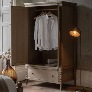 The CHOICEWARDROBE Arta 2 Door Solid Wood Wardrobe in Natural Oak Finish features open doors displaying white shirts on hangers, rolled towels on a shelf, and a bottom drawer. Rustic handcrafted design with turned legs—ideal bedroom storage.
