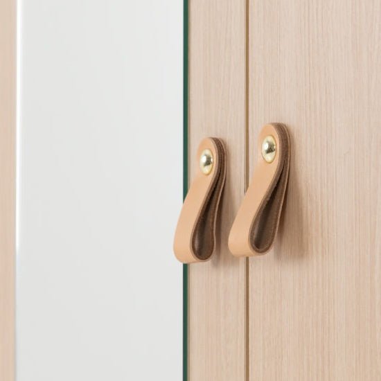 Close-up of two tan leather loop handles with brass fasteners on a wardrobe door.