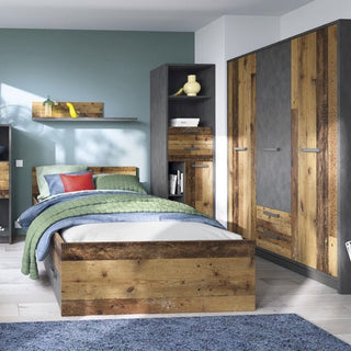 A modern bedroom with a single bed, green bedding, colorful pillows, and a blue area rug features the CHOICEWARDROBE Beeston 3 Door Wardrobe in rustic wood and concrete finish, plus matching shelving. The walls are painted blue and white with light wood flooring.