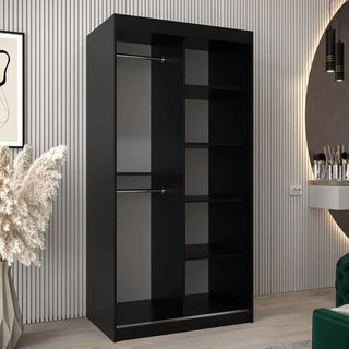 The CHOICEWARDROBE Beloit 2 Door Mirrored Sliding Wardrobe in a 100cm black finish, with geometric mirror and smooth-glide doors, stands in a modern room with light wood floors, ribbed beige wall panels, and minimal decor.