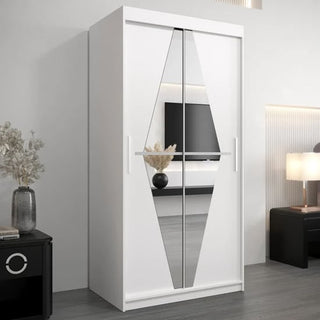 The CHOICEWARDROBE Beloit 2 Door Sliding Mirrored Wardrobe in White Matte Finish with geometric mirror design stands against a light wall. A vase with dried plants sits on a black nightstand, and a lamp rests on another black table nearby.