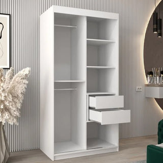 The CHOICEWARDROBE Beloit 2 Door Sliding Mirrored Wardrobe in white matte finish, featuring a stylish geometric mirror design with hanging rail and internal shelving, stands against a modern wall. Decorative items and a green chair are partially visible nearby.