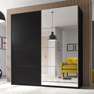 The CHOICEWARDROBE Biella 200cm 2 Door Sliding Mirrored Wardrobe in black stands before vertical wooden slats, its mirrors reflecting a yellow armchair, pendant lamp, and part of a modern living room. Features shelves & hanging rails.