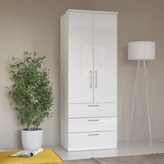 The CHOICEWARDROBE Bristol High Gloss White Wardrobe with LED Lights features 2 doors and 3 drawers, offering modern bedroom storage. It’s shown against a beige wall, beside a green plant, floor lamp, and yellow mat with an open magazine.