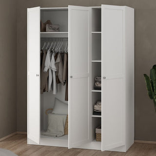 The CHOICEWARDROBE Burbank 3 Door Wooden Wardrobe in a white finish features a minimalist modern design with hanging rail and shelves, shown open with clothes, basket, and pillow. It stands on a wood floor against a taupe wall next to a plant.