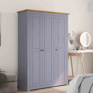 The CHOICEWARDROBE Bury 3 Door Wooden Wardrobe in grey with an oak top stands against the wall beside a wooden dressing table featuring a round mirror and decorative items, creating stylish, spacious bedroom storage.