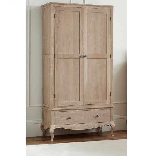 The CHOICEWARDROBE Caitlyn Wooden Wardrobe in an oak finish, with 2 paneled doors, a spacious bottom drawer, elegant curved legs, and antique metal handles, stands against a cream-colored wall.