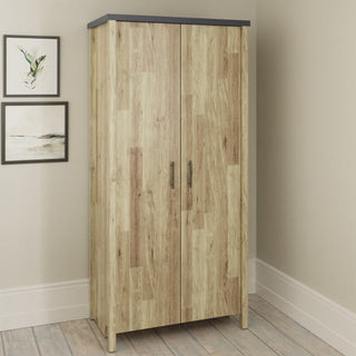 The CHOICEWARDROBE Calgary Rustic Oak 2 Door Wardrobe with graphite trim stands against a beige wall, its light wood finish and dark top complemented by black handles. Two framed pictures hang to the left of the wardrobe.