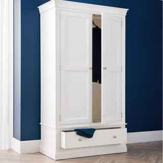 The CHOICEWARDROBE Calida 2 Door Wooden Wardrobe in Lacquer White, featuring elegant panel detailing and a deep lower drawer, stands against a blue wall on a light wooden floor with clothing visible inside.