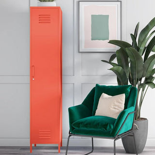 A CHOICEWARDROBE Cerritos 38cm 1 Door Metal Locker in Industrial Orange stands beside a framed abstract artwork and large green plant. A green velvet armchair with a beige pillow is next to the locker.