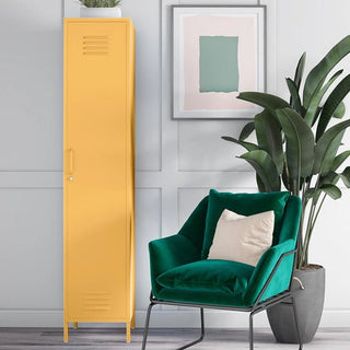 A CHOICEWARDROBE Cerritos 38cm Metal Single Door Wardrobe in yellow stands beside a green velvet armchair and large potted plant, with abstract artwork on a light gray paneled wall in this modern room.