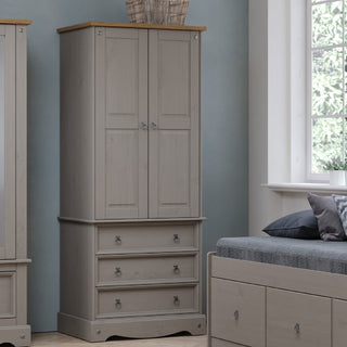 The CHOICEWARDROBE Consett Wooden Wardrobe – 2 Doors & 3 Drawers in Grey with Oak Top (76.5cm wide) stands next to a window and gray bed in a light blue room, with a wicker basket placed on top.