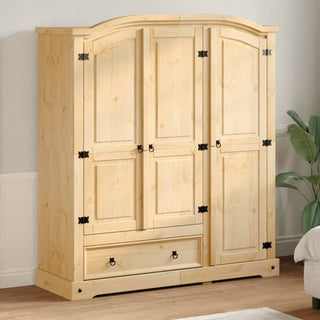 The CHOICEWARDROBE Croydon Grand 3 Door Pine Wardrobe with Drawer, featuring an arched top and black iron detailing, stands against a light-colored wall beside a green plant.