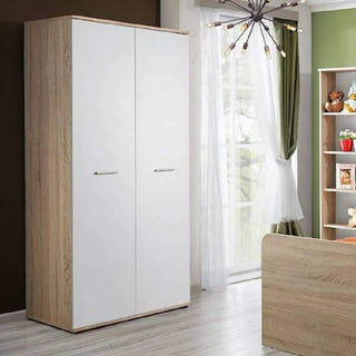 A CHOICEWARDROBE Dania 2 Door Wardrobe – White & Oak Effect 90cm, a compact modern storage piece, stands in a bright room with light wood floors by a window with sheer curtains and green drape; shelving unit and bed are partly visible.