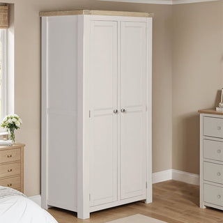 The CHOICEWARDROBE Dawson 2 Door Wooden Wardrobe in taupe and oak finish stands by the window of a beige bedroom, near a matching dresser. A flower vase on the nightstand adds charm to the organized storage space.