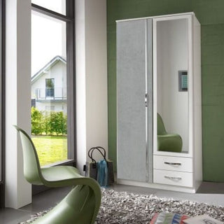 A modern room with a green chair, a CHOICEWARDROBE Dayton 2 Door 2 Drawer Mirrored Wardrobe (90 cm, white & concrete grey), a gray rug, two bags on the floor, large windows, and views of a house amid greenery.