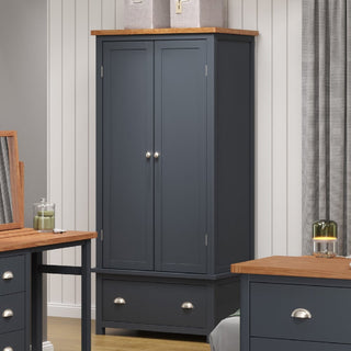 The CHOICEWARDROBE Delavan 2 Door Wooden Wardrobe in navy and oak finish, featuring classic design, drawer storage, and metal handles, is placed in a room with light walls and matching furniture.