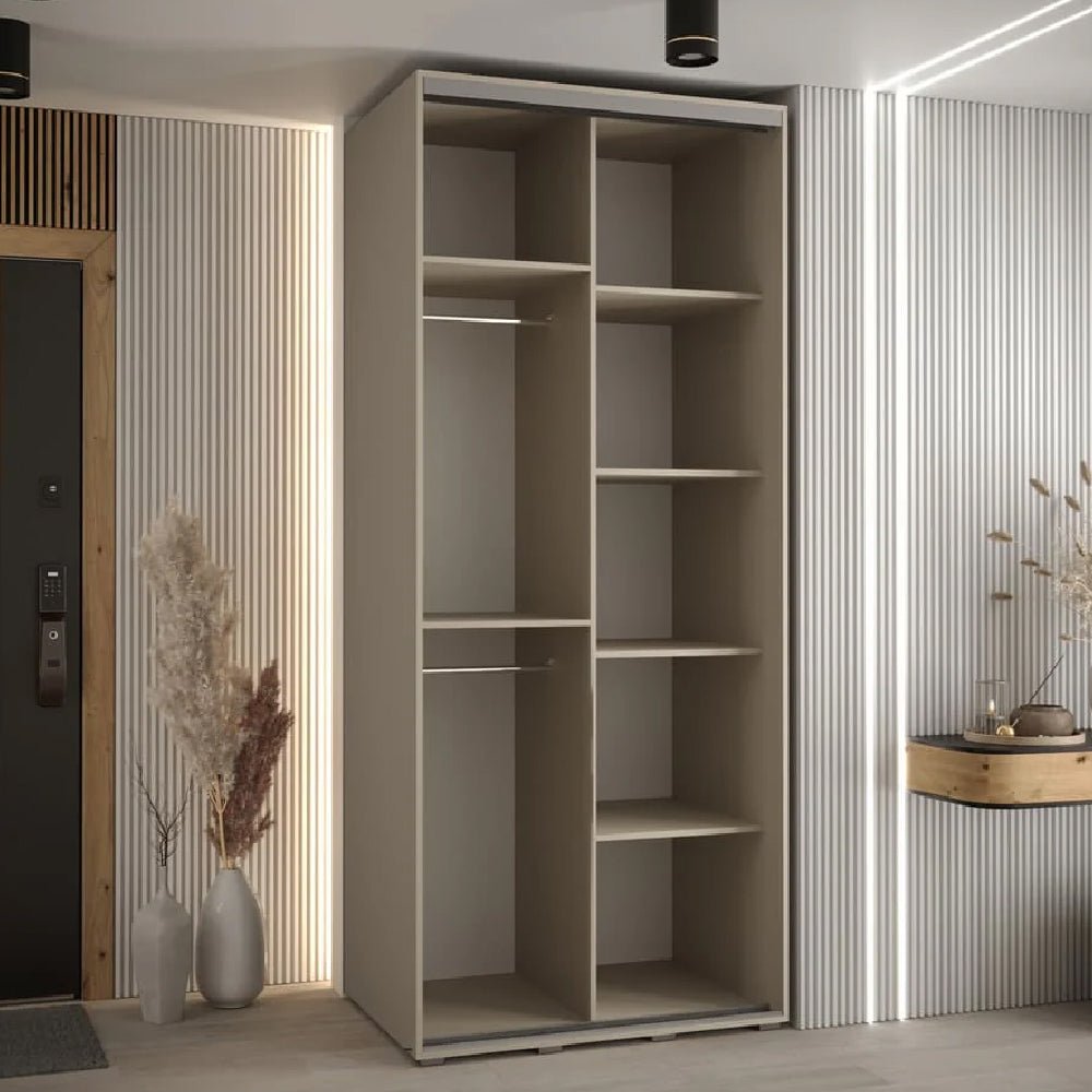 The CHOICEWARDROBE Delta 100cm 2 Door Sliding Wardrobe in a cashmere finish with black trim stands against a light wall, complemented by dried plants in vases on the left and a small wooden floating shelf with a vase on the right.
