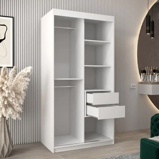The CHOICEWARDROBE Eden 100cm White Mirrored Sliding Door Wardrobe features a modern curved mirror, spacious shelves, and a hanging rail. It stands in a stylish room with striped walls, pampas grass in a vase, a round mirror, and chic bedroom furniture.