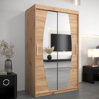 The CHOICEWARDROBE Eden 120cm Artisan Oak Mirrored Wardrobe features elegant curved mirror panels and premium storage shelving, providing stylish bedroom storage in a modern room with a TV, lamp, nightstand, and decor accents.