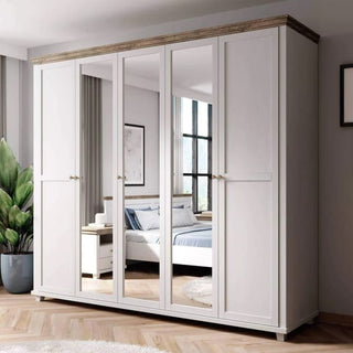 The CHOICEWARDROBE Eilat 246cm 5 Door Mirrored Wardrobe in Abisko Ash, featuring a classic panel design and ample storage, stands in a bedroom with a bed, nightstand, large window, potted plant, wooden floors, and neutral walls.