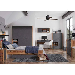 A modern bedroom with wooden furniture, a bed, desk with computer, shelves, white chair, gray rug, ceiling fan, and large windows. The CHOICEWARDROBE Fairbourne L-Shaped Corner Wardrobe adds industrial walk-in style. A brown bag sits on the floor by the bed.