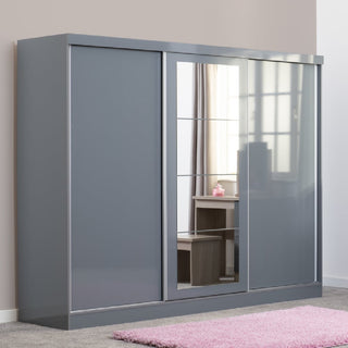 The CHOICEWARDROBE Grey Gloss 3 Door Sliding Wardrobe with Mirror (242.5cm wide) features a modern design with sliding doors, a central mirrored panel reflecting the room, and is placed on grey carpet with a pink rug in front.