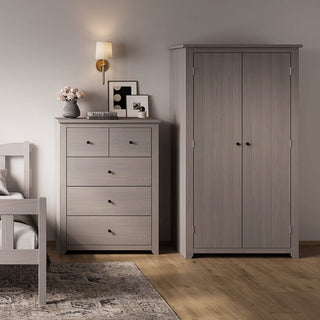 A bedroom corner with a gray wooden dresser and a CHOICEWARDROBE Havanan 2 Door Wooden Wardrobe in matte grey, plus part of a bed, wall sconce, framed photos, vase with flowers, and patterned rug on light wood flooring from Furniture In Fashion.
