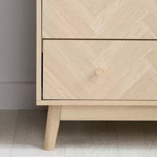 A close-up of the CHOICEWARDROBE Helena 90cm 2 Door Wooden Wardrobe in natural oak with a chevron pattern front, a drawer, and Scandinavian tapered legs. The lower left corner of the wardrobe and part of the floor are visible.