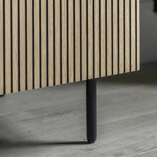 Close-up of the CHOICEWARDROBE Helena Wooden Wardrobe—2 Door Natural Oak Finish with ribbed panel design, black metal legs, and minimalist handles—positioned on a light wooden floor.