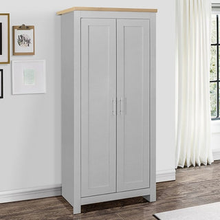 The CHOICEWARDROBE Highgate 2 Door Wardrobe in grey with an oak top stands on a dark wood floor by a white wall, next to framed pictures and a window with white curtains. It features silver handles and compact modern storage (79cm wide).